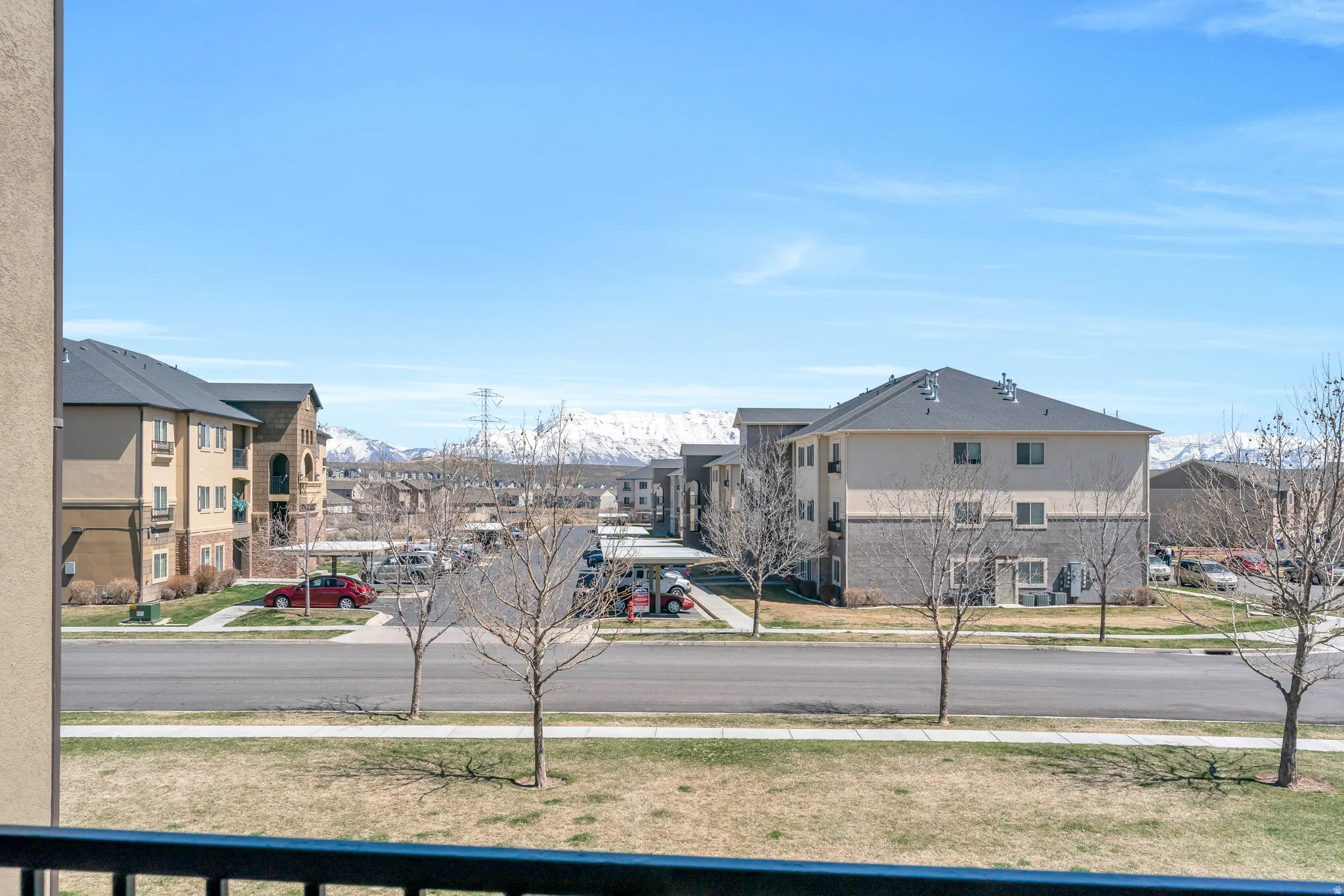 Balcony with metal railing offering elevated views of the streetscape and distant snow-capped mountains