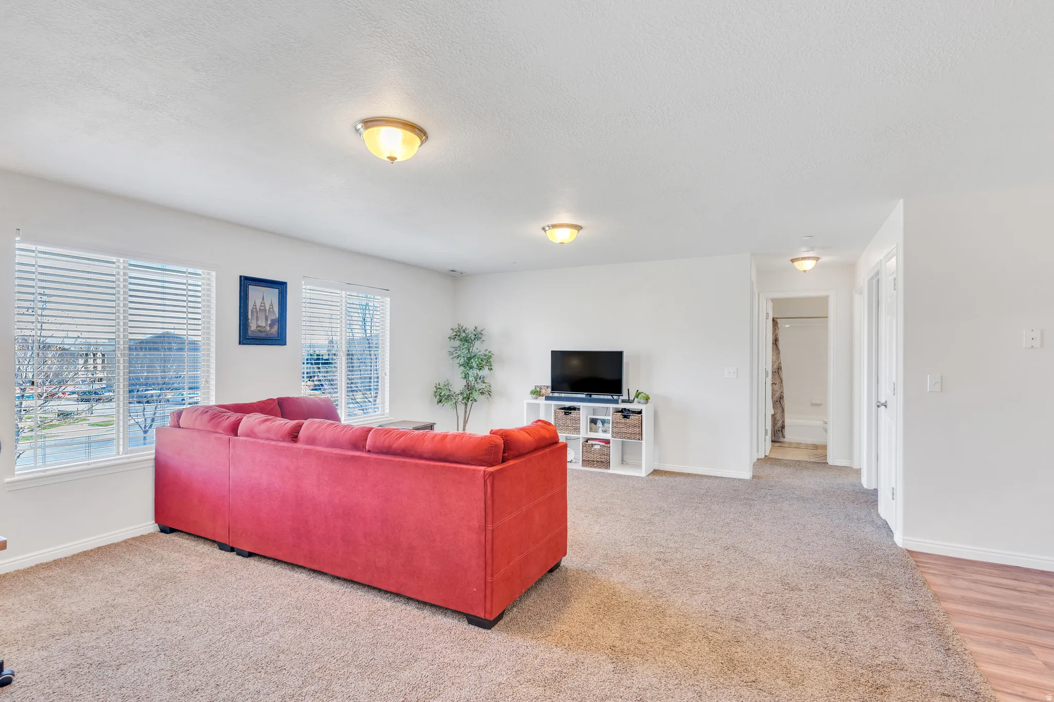 Spacious common area featuring light brown carpet, multiple windows with blinds, and recessed lighting fixtures