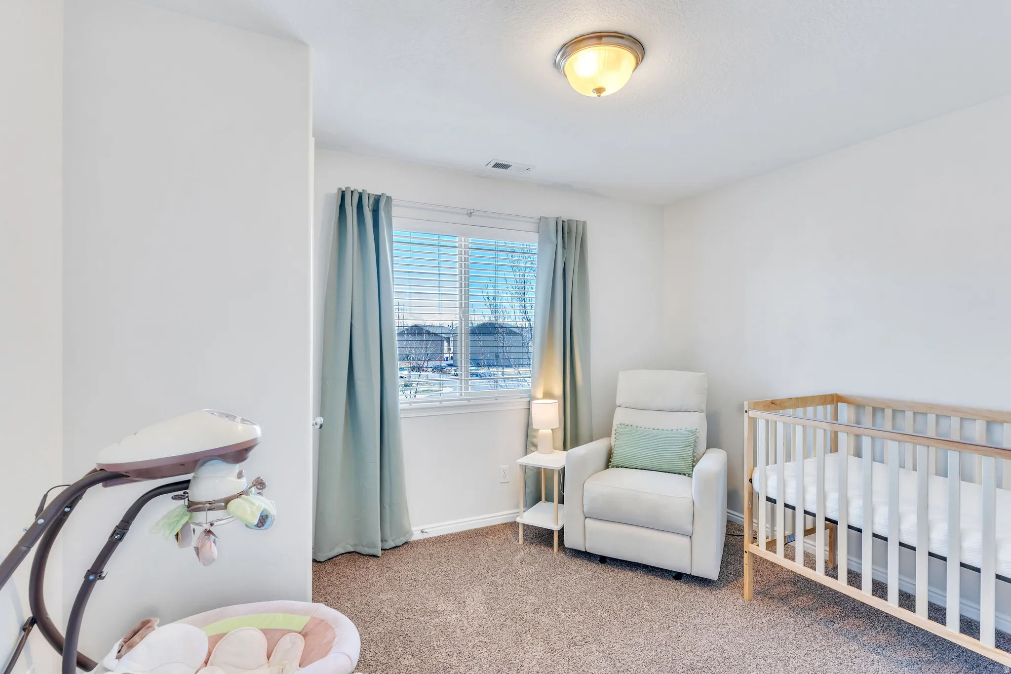 Bright interior room featuring neutral-toned walls, textured carpeting, and a window with blinds and drapes