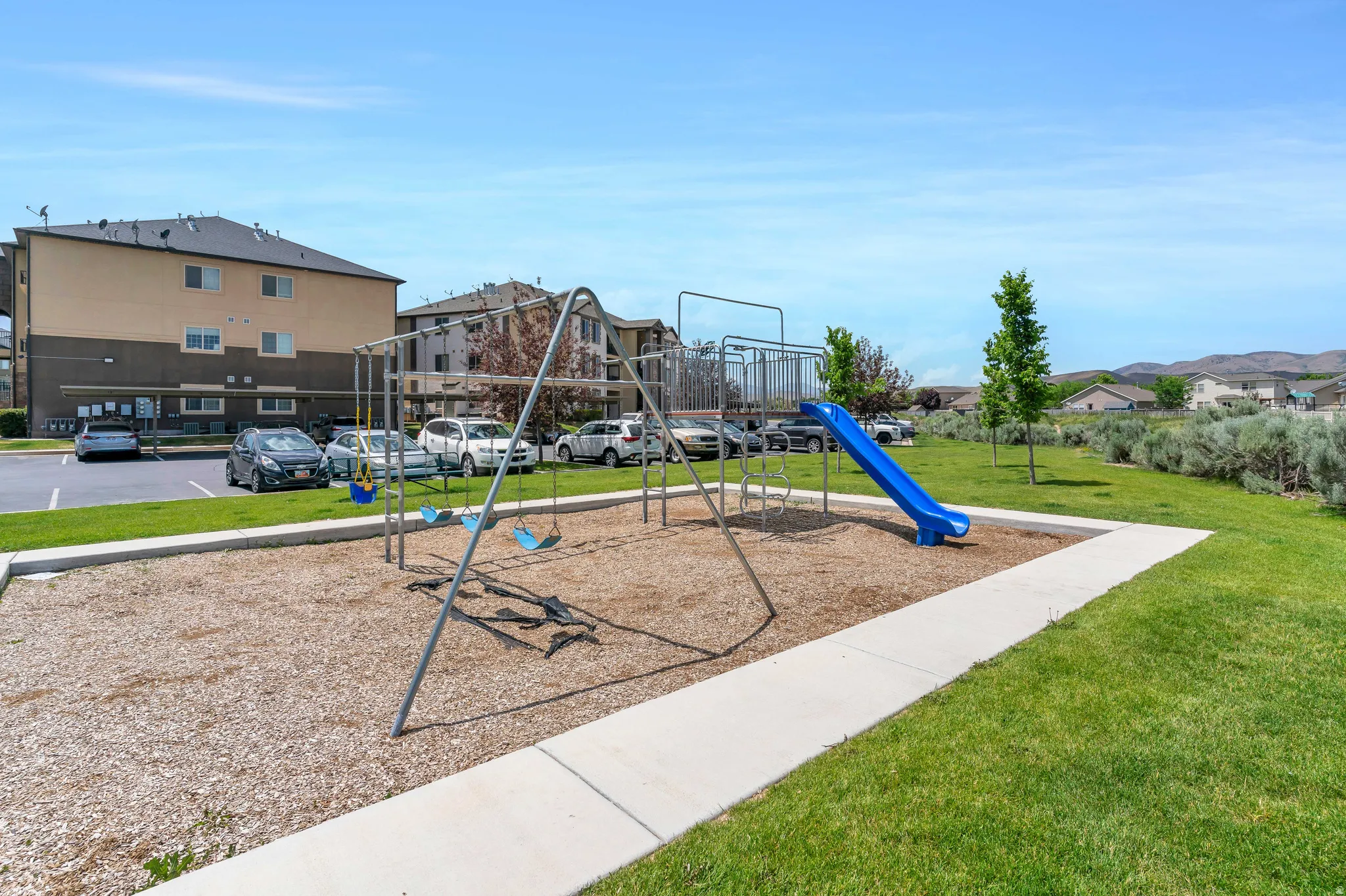 On-site playground featuring a swing set and slide, surrounded by green space, with a paved walkway