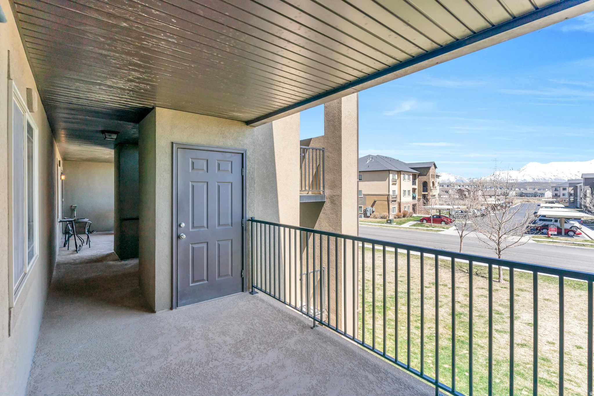 Covered balcony with a six-panel entry door, concrete flooring, and metal railing