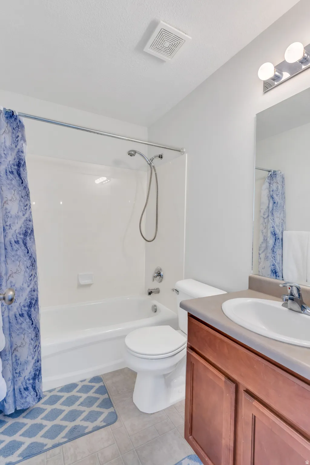 Full bathroom featuring a white tub/shower combination with chrome fixtures, a white toilet, and a wood-finish vanity with an integrated sink and countertop