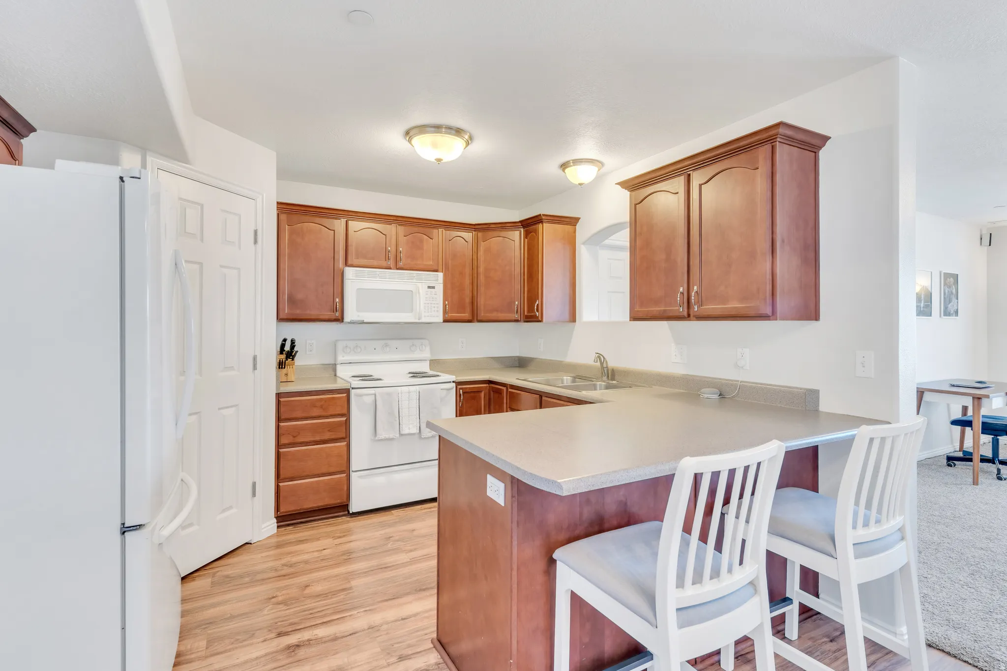 Kitchen featuring wood-finish flooring, warm wood cabinetry, light-toned countertops, and a breakfast bar