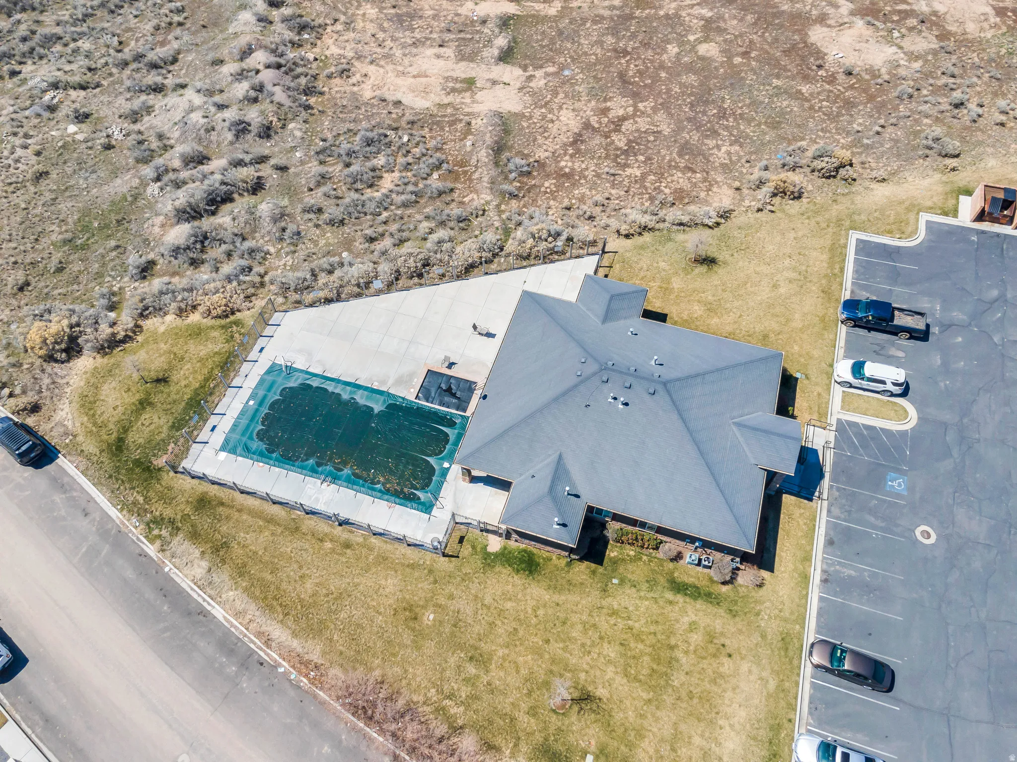 Building with a dark grey shingle roof, surrounded by a concrete patio and a covered swimming pool
