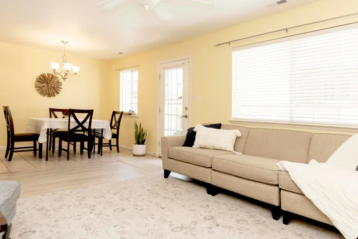 Open-concept living and dining area featuring wood-finish flooring, a ceiling fan with light, and multiple windows with horizontal blinds