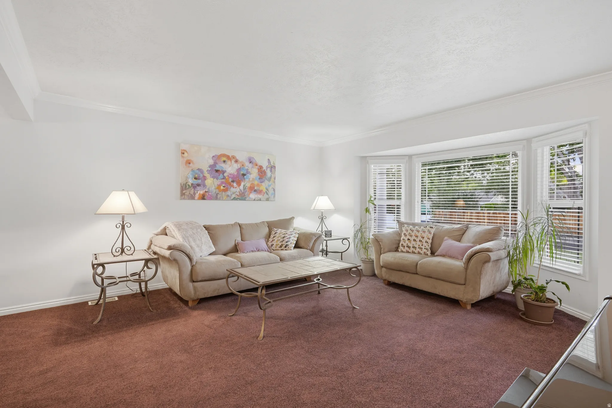 Living room featuring a large bay window, crown molding, white walls, and plush carpeting in actual color.