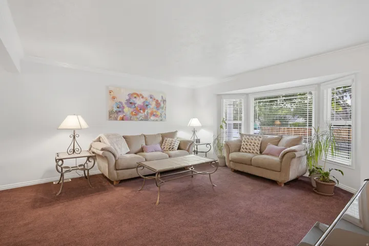 Living room featuring a large bay window, crown molding, white walls, and plush carpeting in actual color.