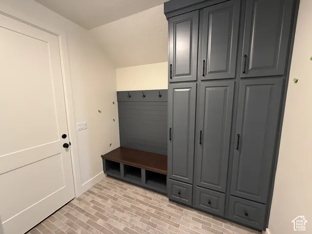 Built-in storage area featuring dark-finished cabinetry with matte black hardware, integrated bench seating with open shelving, wall-mounted hooks, shiplap detailing, and neutral-toned tile flooring
