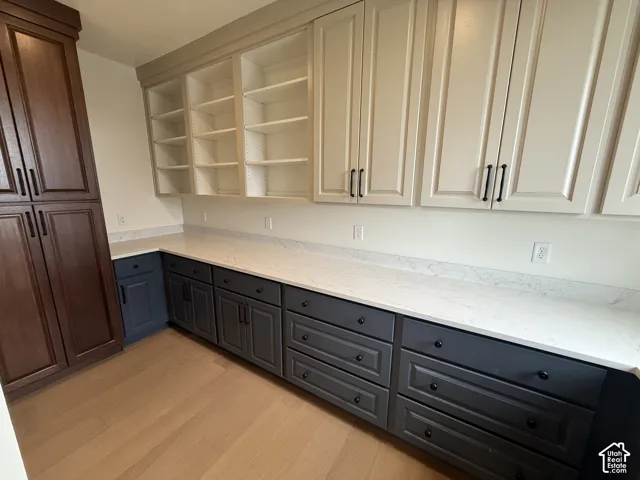 Custom built-in cabinetry featuring a mix of dark wood-finish and charcoal-toned lower cabinets, complemented by light-toned upper cabinetry, stone-composite countertops, and wood-finish flooring