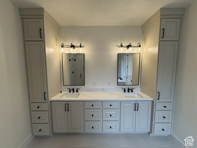Double vanity featuring stone-finish countertops, undermount sinks, custom floor-to-ceiling cabinetry, dual rectangular mirrors with dark frames, and matte black fixtures
