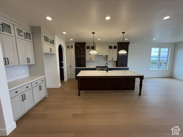 Kitchen featuring wood-finish flooring, dual-tone cabinetry, a central island with a quartz countertop, recessed lighting, and pendant fixtures