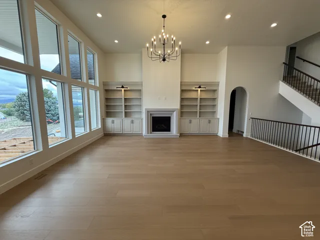 Expansive living space featuring wood-finish flooring, floor-to-ceiling windows, a central fireplace with built-in cabinetry, and an ornate chandelier