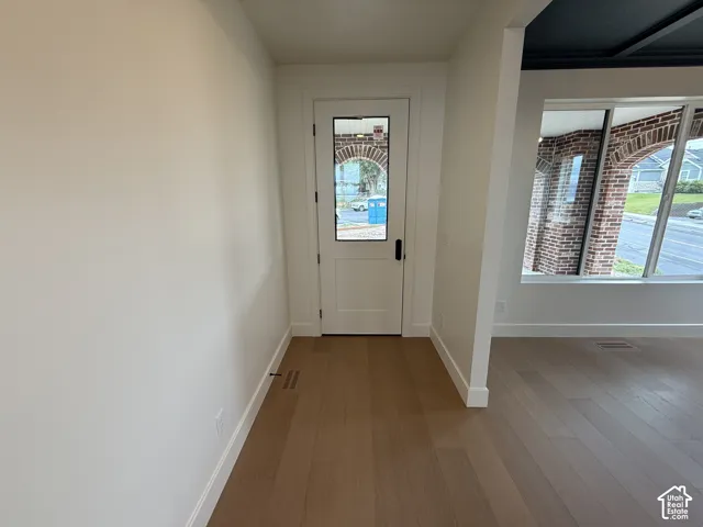 Entryway featuring wood-finish flooring, a single-panel door with a glass insert, and expansive windows with brick masonry trim
