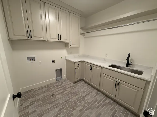 Laundry room featuring light-toned cabinetry, stone-finish countertops, stainless steel undermount sink, matte black hardware, and brick-patterned flooring