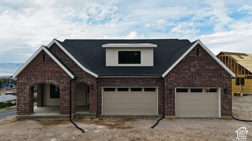 Brick exterior with white trim, arched portico, two-car garage, and dark shingle roof