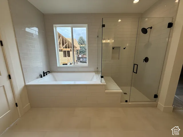 Deep soaking tub and separate glass-enclosed shower with matte black fixtures, tile surround, and built-in bench