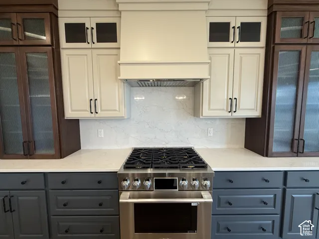 Chef's kitchen featuring dual-tone cabinetry with cream upper cabinets and charcoal lower drawers, stainless steel six-burner gas range with matching hood, white quartz countertops, and marble subway tile backsplash
