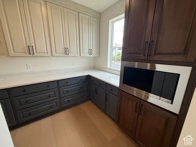 Custom cabinetry featuring two-tone charcoal and off-white finishes, complemented by wood-finish flooring, quartz countertops, and a built-in stainless steel microwave