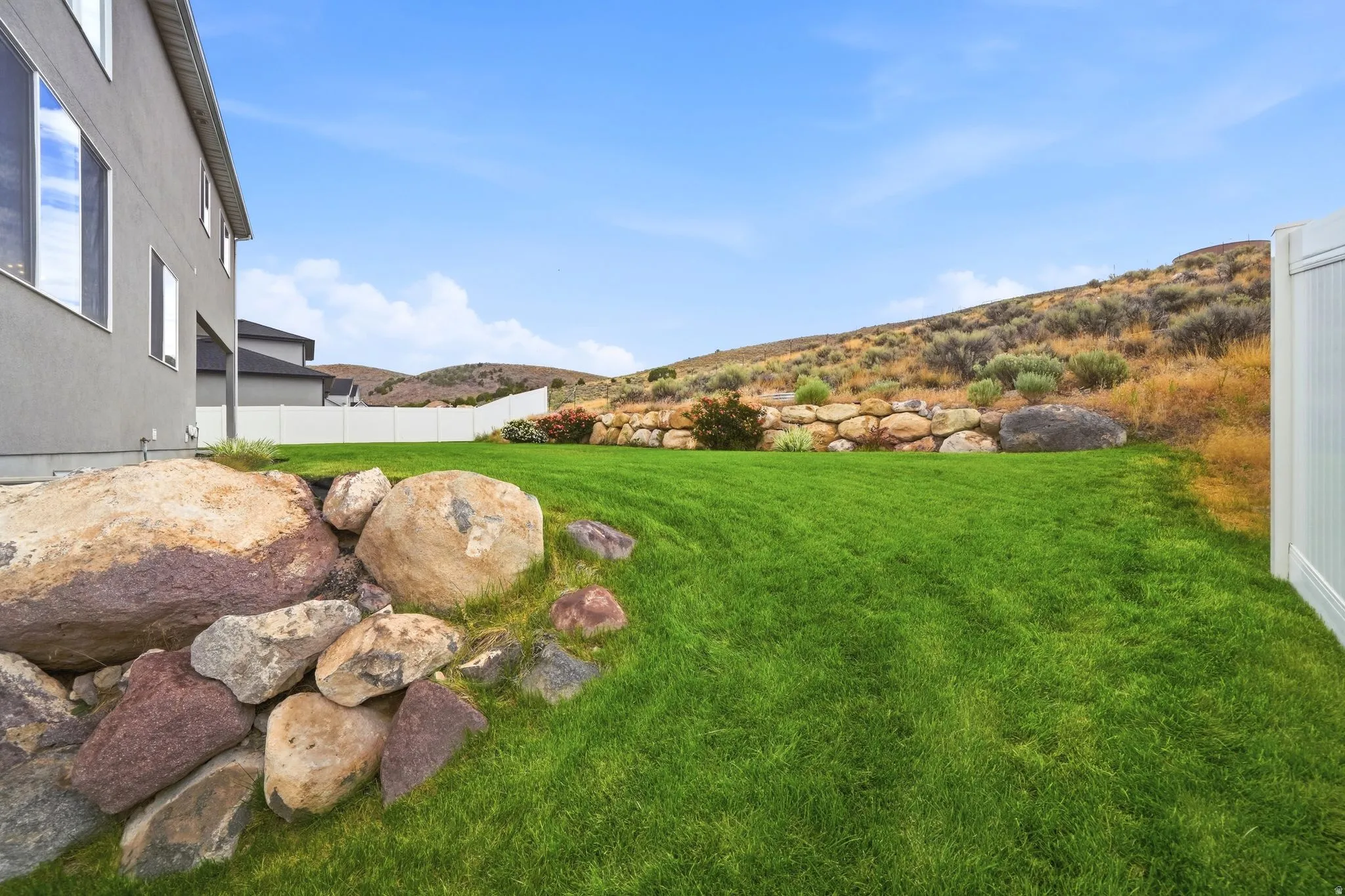 Expansive backyard featuring a manicured lawn, a white privacy fence, and a rock retaining wall