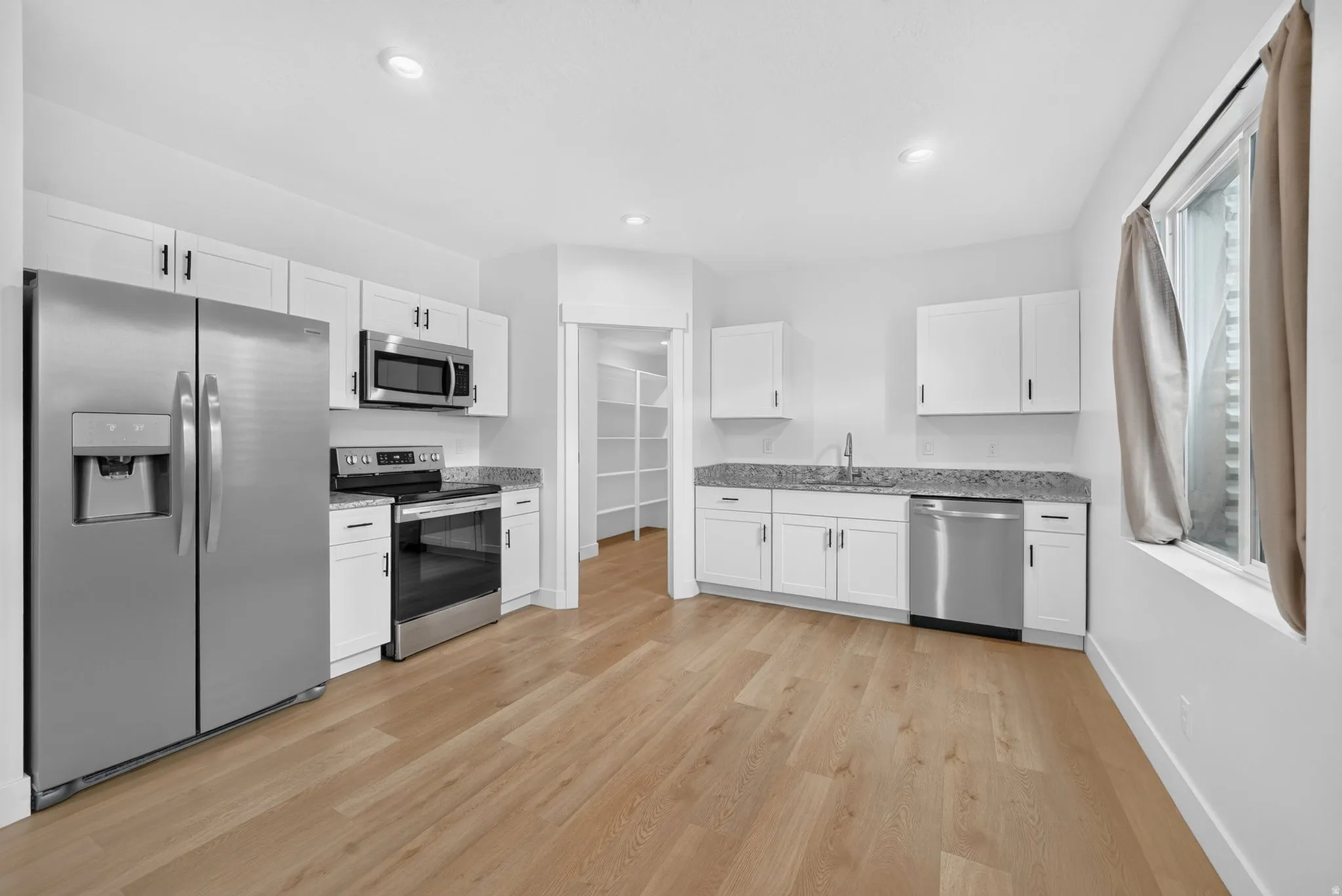 Bright kitchen featuring white cabinetry, stainless steel appliances, speckled countertops, wood-finish flooring, and a walk-in pantry