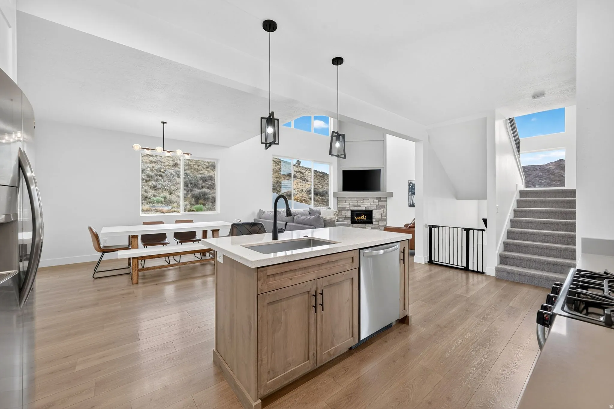 Open-concept living area featuring a kitchen island with sink, stainless steel appliances, wood-finish flooring, and a fireplace with stone surround