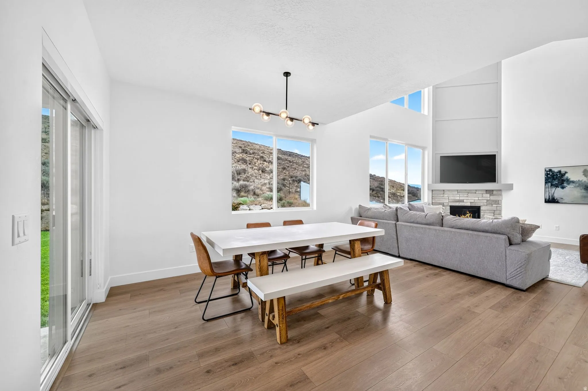 Open-concept interior featuring wood-finish flooring, a modern linear chandelier, and expansive windows