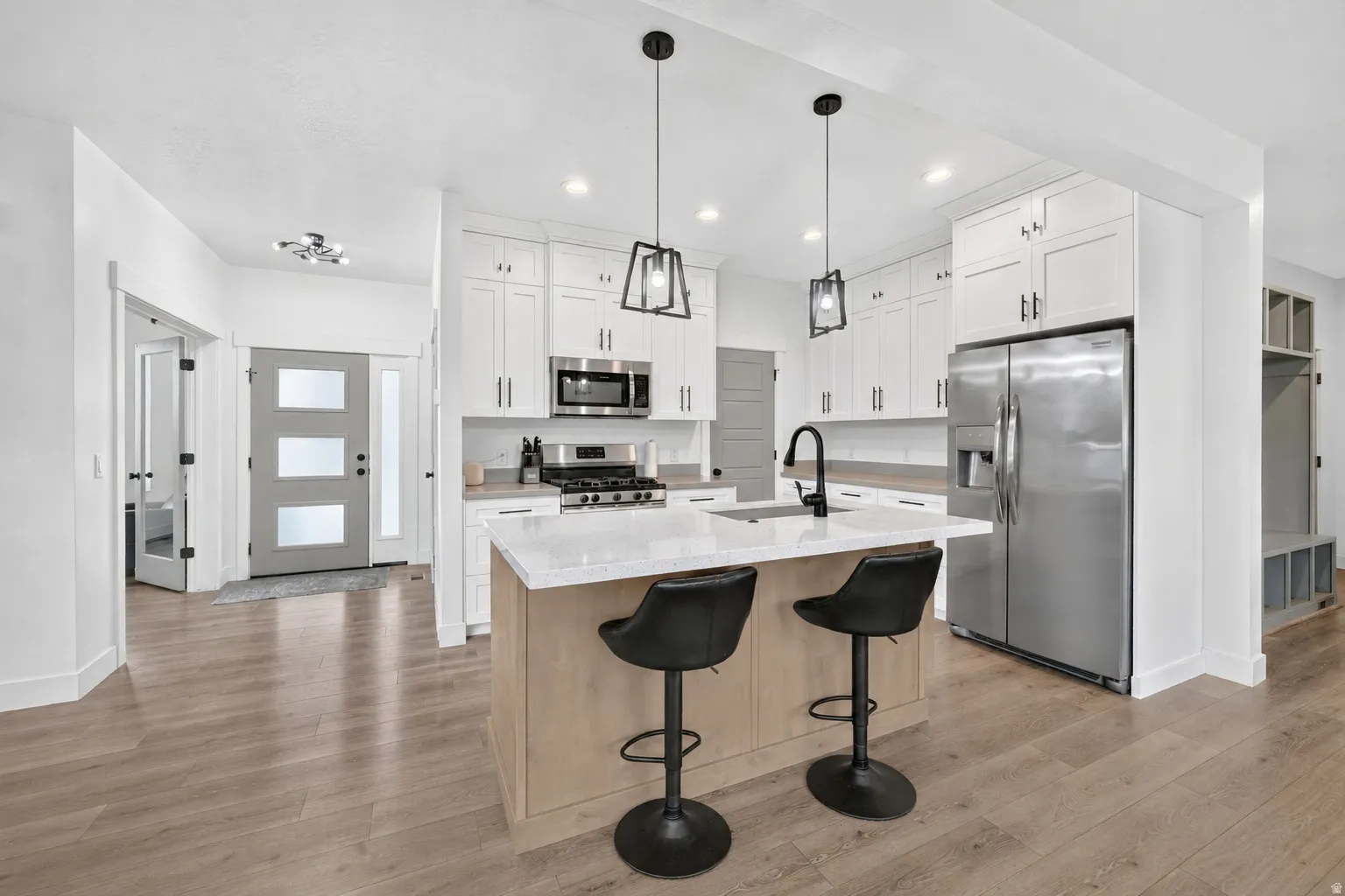 Open-concept kitchen featuring an island with seating, stacked shaker cabinetry, stainless steel appliances, and wood-finish flooring