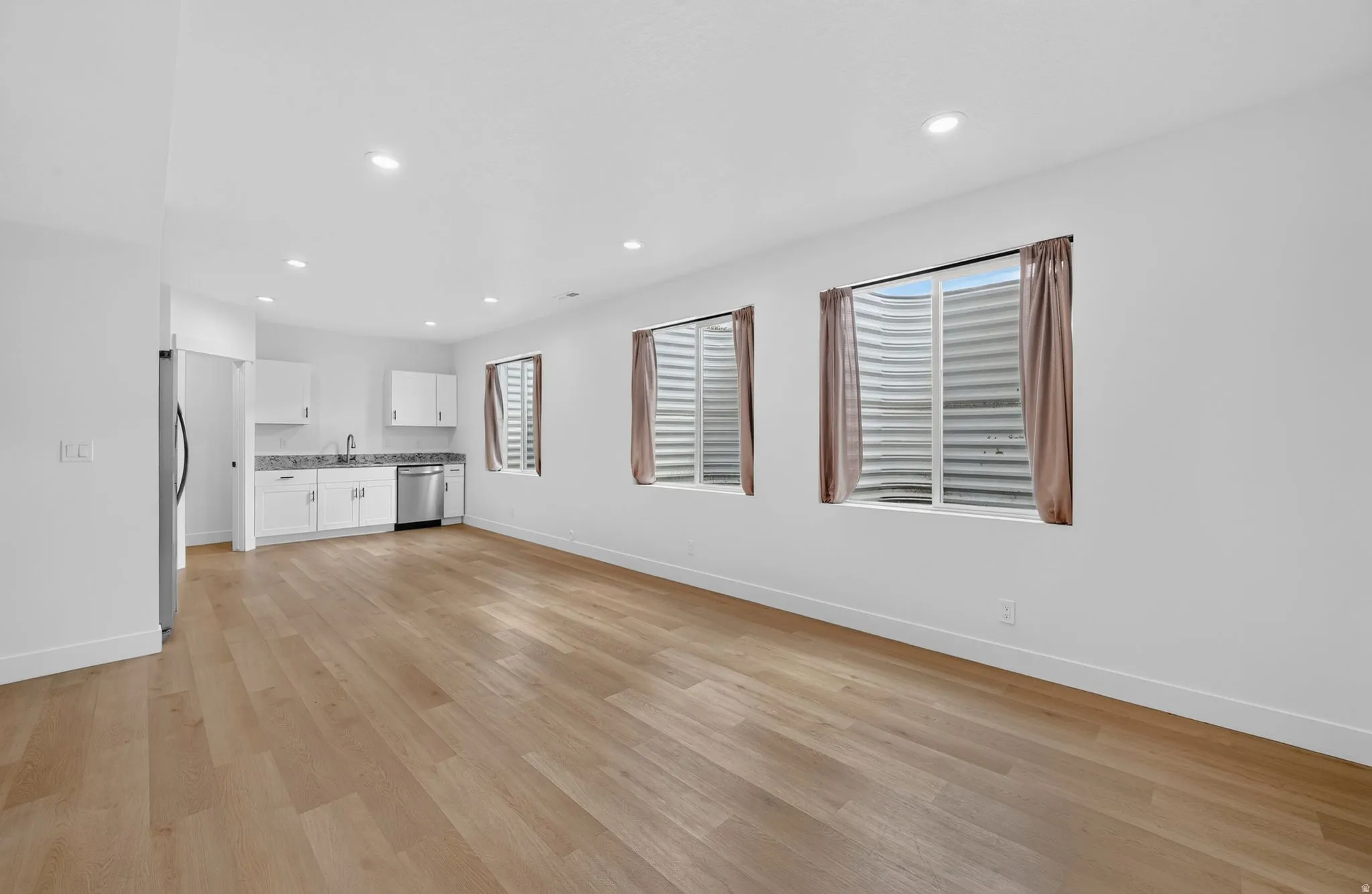 Open-concept living space featuring wood-finish flooring, recessed lighting, and a kitchen area with white cabinetry, granite countertops, and stainless steel appliances