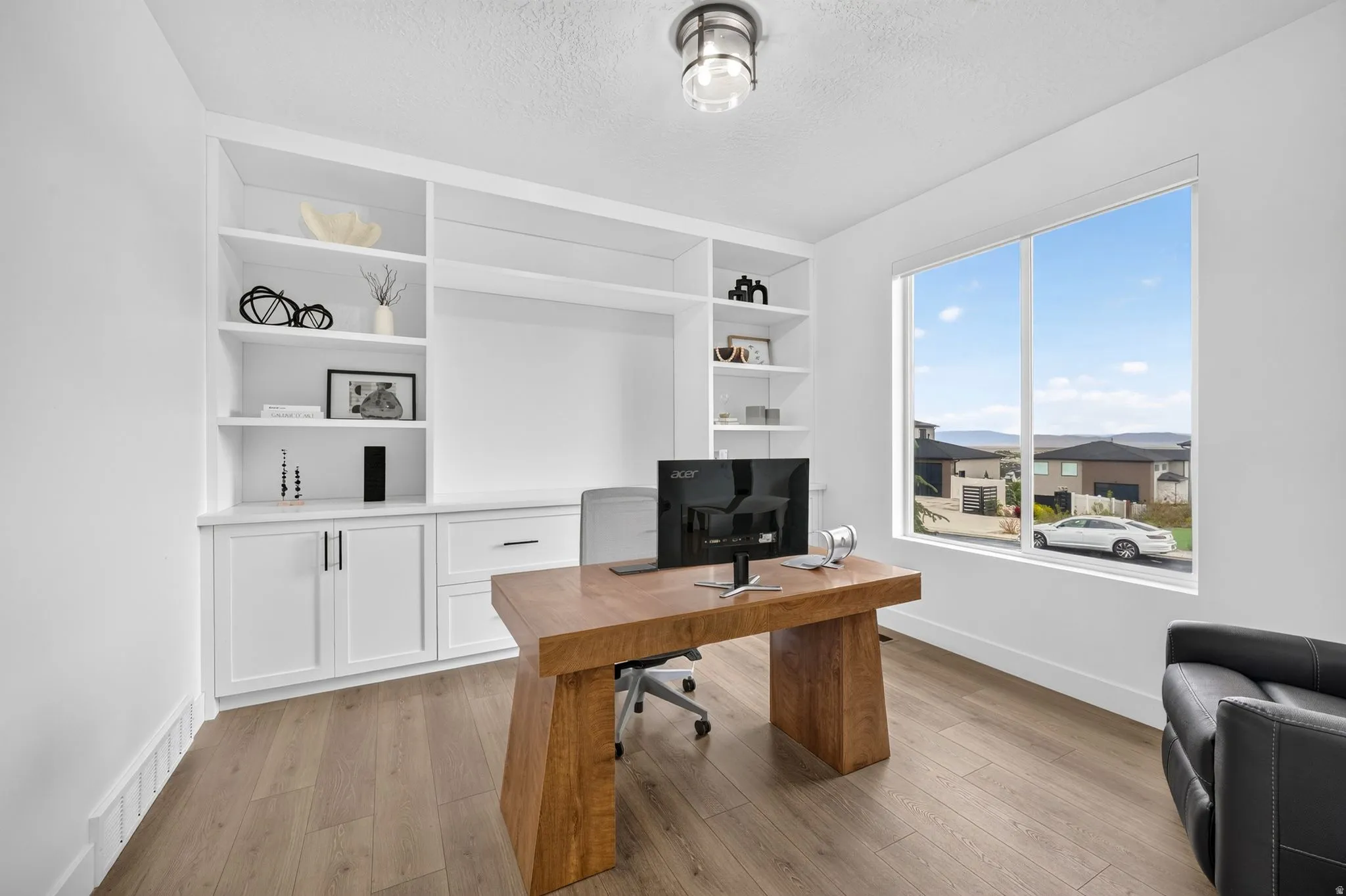Bright room featuring a large picture window, built-in white shelving, integrated cabinetry, wood-finish flooring, and a contemporary ceiling light fixture