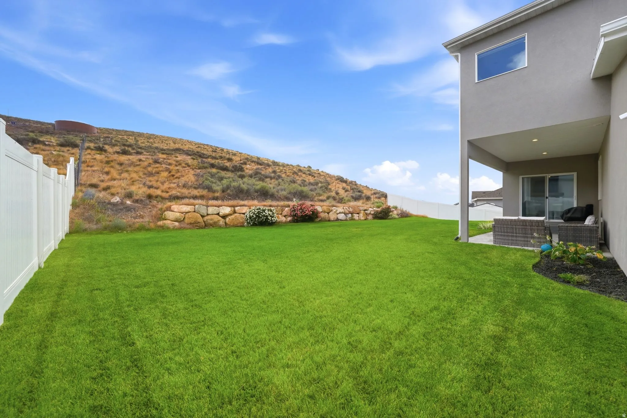 Expansive lawn area featuring a white vinyl fence and a stone retaining wall