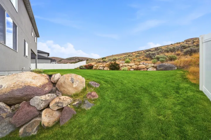 Expansive backyard featuring a manicured lawn, a white privacy fence, and a rock retaining wall