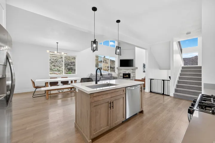 Open-concept living area featuring a kitchen island with sink, stainless steel appliances, wood-finish flooring, and a fireplace with stone surround