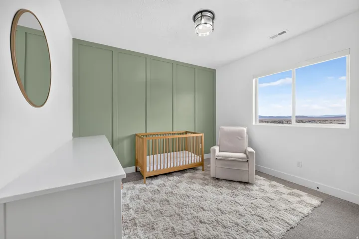 Second-floor bedroom featuring a green accent wall with vertical paneling, white walls, and a large window