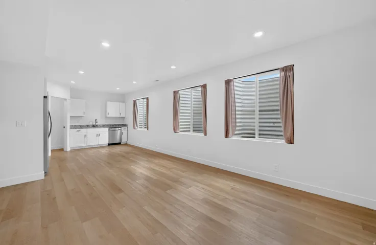 Open-concept living space featuring wood-finish flooring, recessed lighting, and a kitchen area with white cabinetry, granite countertops, and stainless steel appliances