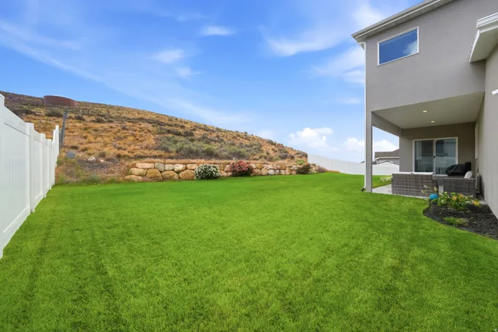 Expansive lawn area featuring a white vinyl fence and a stone retaining wall