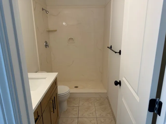 Integrated shower and tub combination with a neutral-toned surround, tiled flooring, wood-finish vanity with white countertop, and contemporary black hardware
