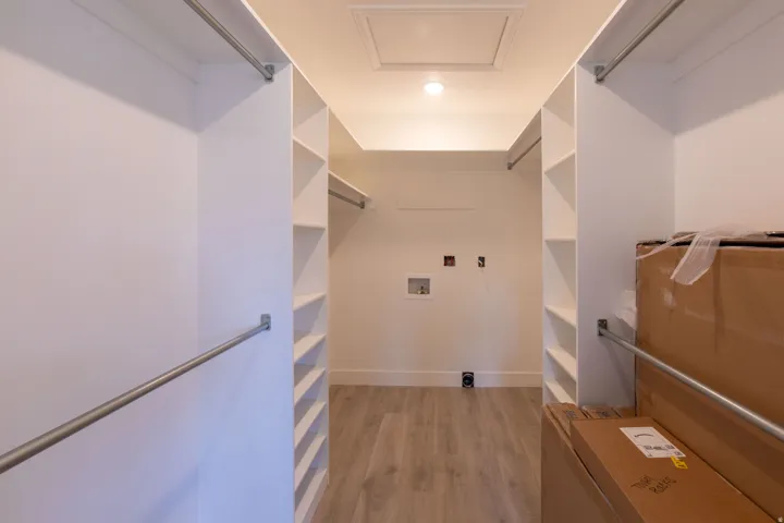 Spacious walk-in closet featuring white built-in shelving, chrome hanging rods, and wood-finish flooring