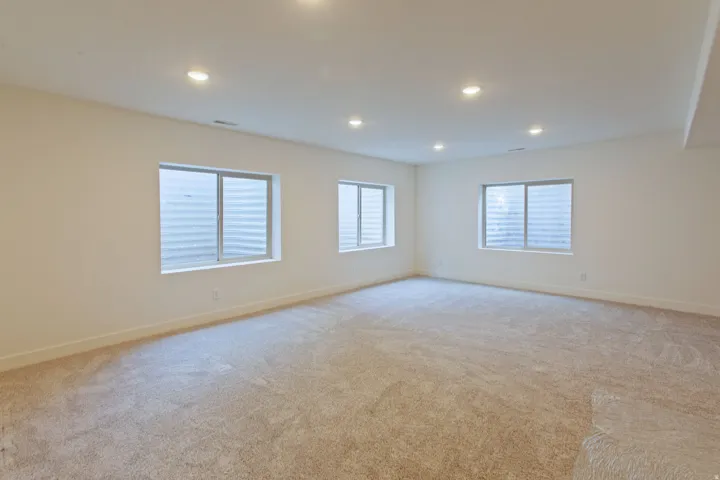 Spacious room featuring new carpet flooring, recessed lighting, and multiple egress windows with white trim