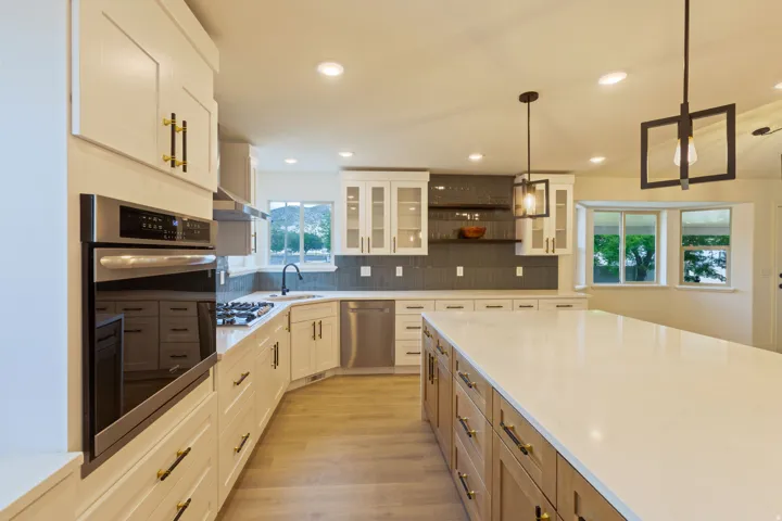 Modern kitchen featuring a large central island with a light-toned countertop, integrated wall oven, stainless steel appliances, white cabinetry with gold-toned hardware, and recessed lighting