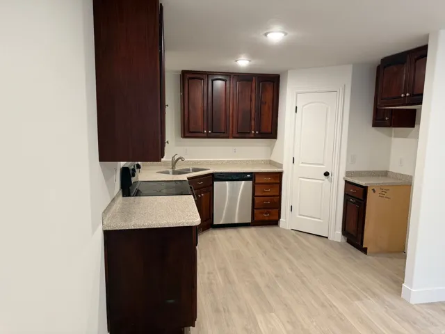 Kitchen featuring dark wood-finish cabinetry, light-toned countertops, stainless steel dishwasher, black electric range, and wood-finish flooring