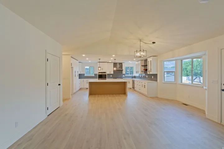 Spacious open-concept living area featuring light wood-finish flooring, a vaulted ceiling, and recessed lighting