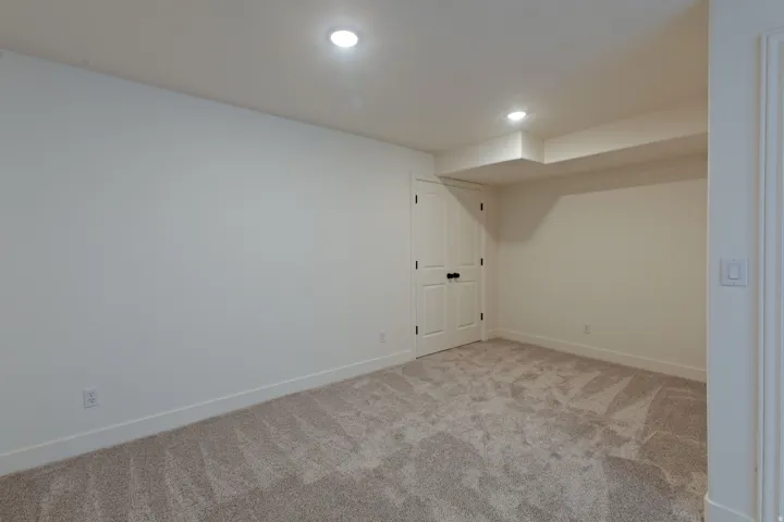 Carpeted room featuring recessed lighting, a white paneled door with dark hardware, and a ceiling soffit