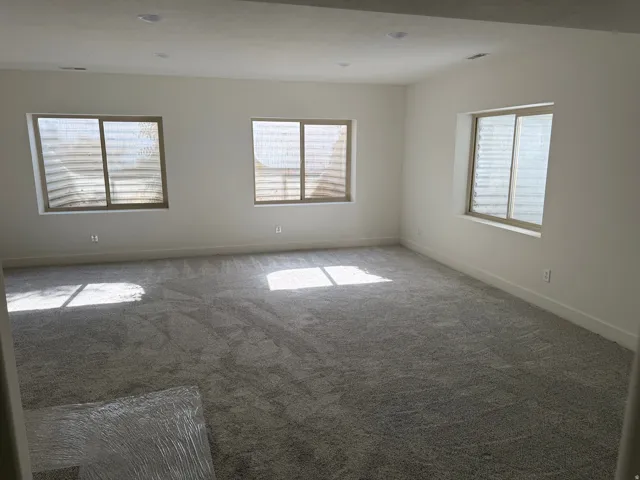 Spacious room featuring neutral carpeting, recessed lighting, and multiple windows with horizontal blinds