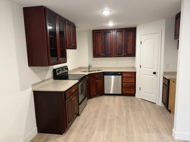 Wood-finish flooring, dark wood cabinetry with select glass-front doors, light-toned countertops, and stainless steel appliances