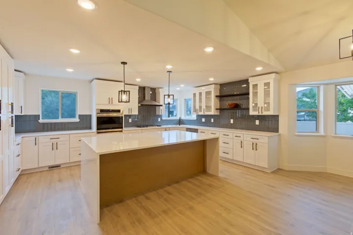 Spacious open-concept kitchen featuring a large central island with a waterfall countertop, white cabinetry with dark hardware, full-height subway tile backsplash, and wood-finish flooring