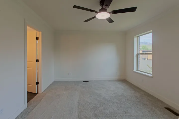 Carpeted room featuring a ceiling fan with integrated lighting, white walls, and a window with mountain scenery
