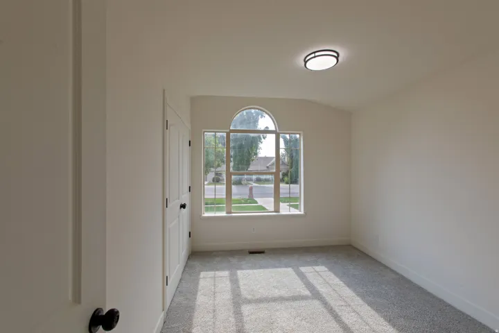Room featuring a large arched window, vaulted ceiling, neutral wall color, gray carpet, and a modern flush-mount ceiling light