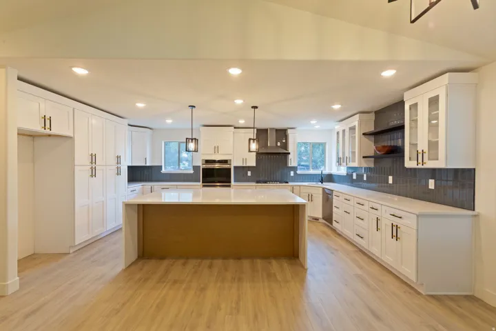 Spacious kitchen featuring an expansive central island, white cabinetry with dark hardware, a dark tile backsplash, recessed lighting, and wood-finish flooring