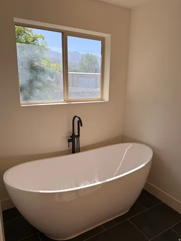 Freestanding soaking tub with a matte black floor-mounted faucet, set on dark tile flooring