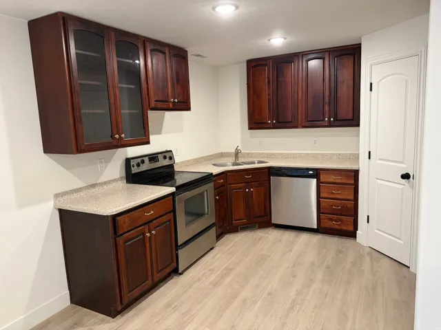 Wood-finish flooring, dark wood cabinetry with glass-front uppers, stainless steel appliances, and solid surface countertops